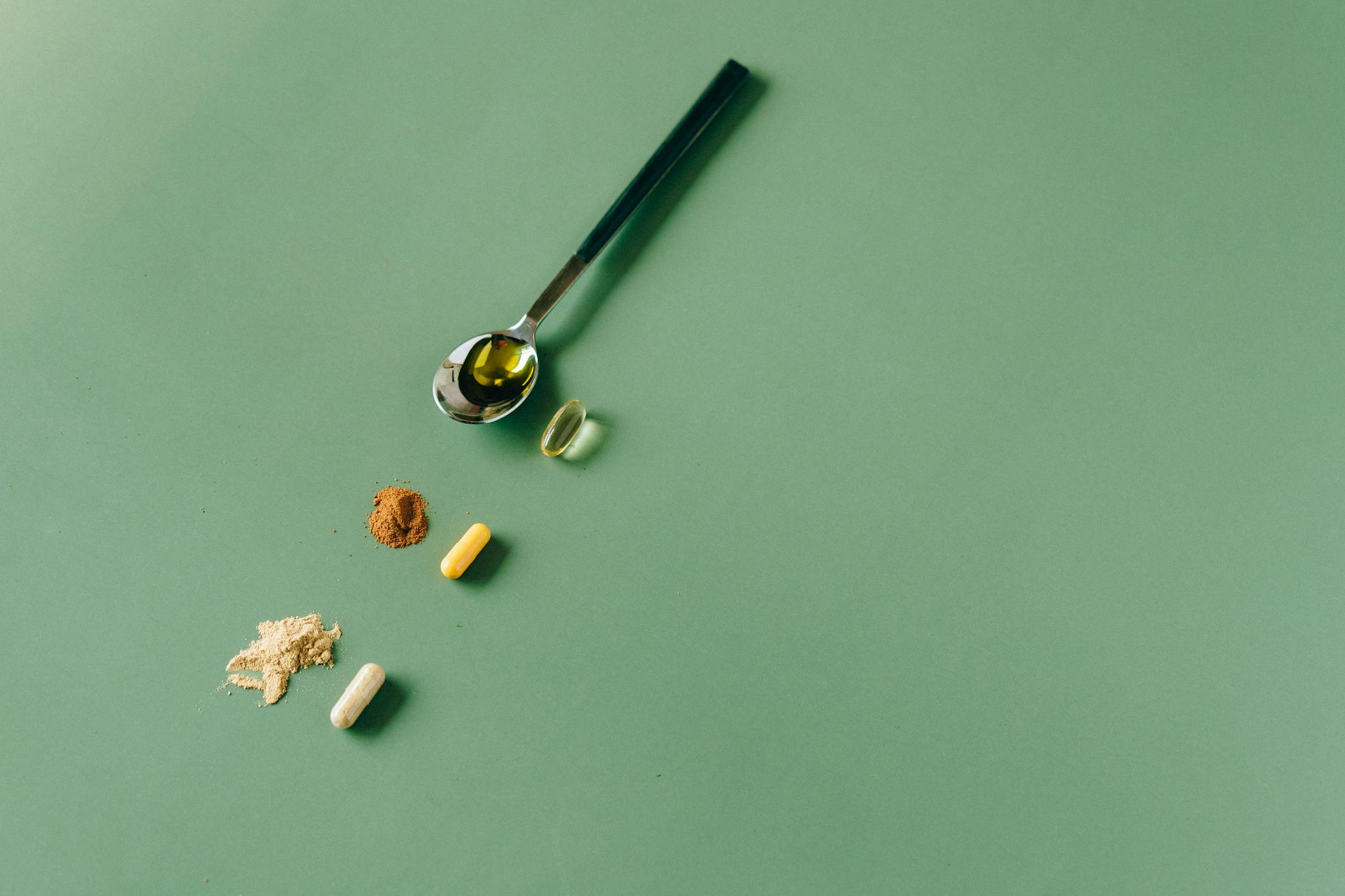 Assorted herbal supplements and powders on a green backdrop with a spoon.